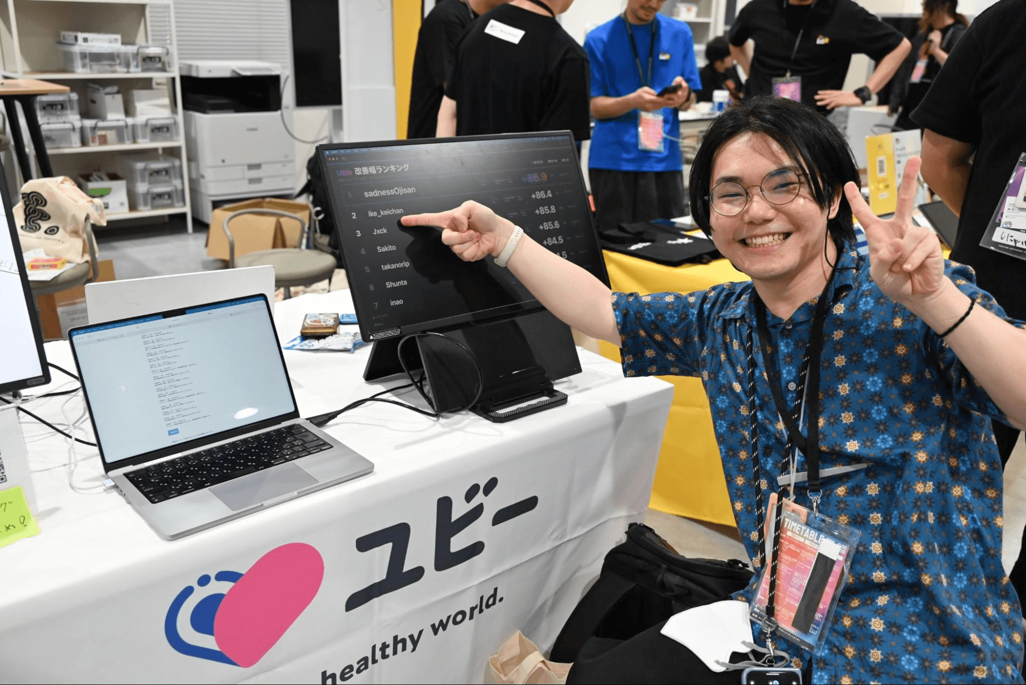 ユビーのブースで、AIによるコード改善幅のランキング画面を指さす参加者