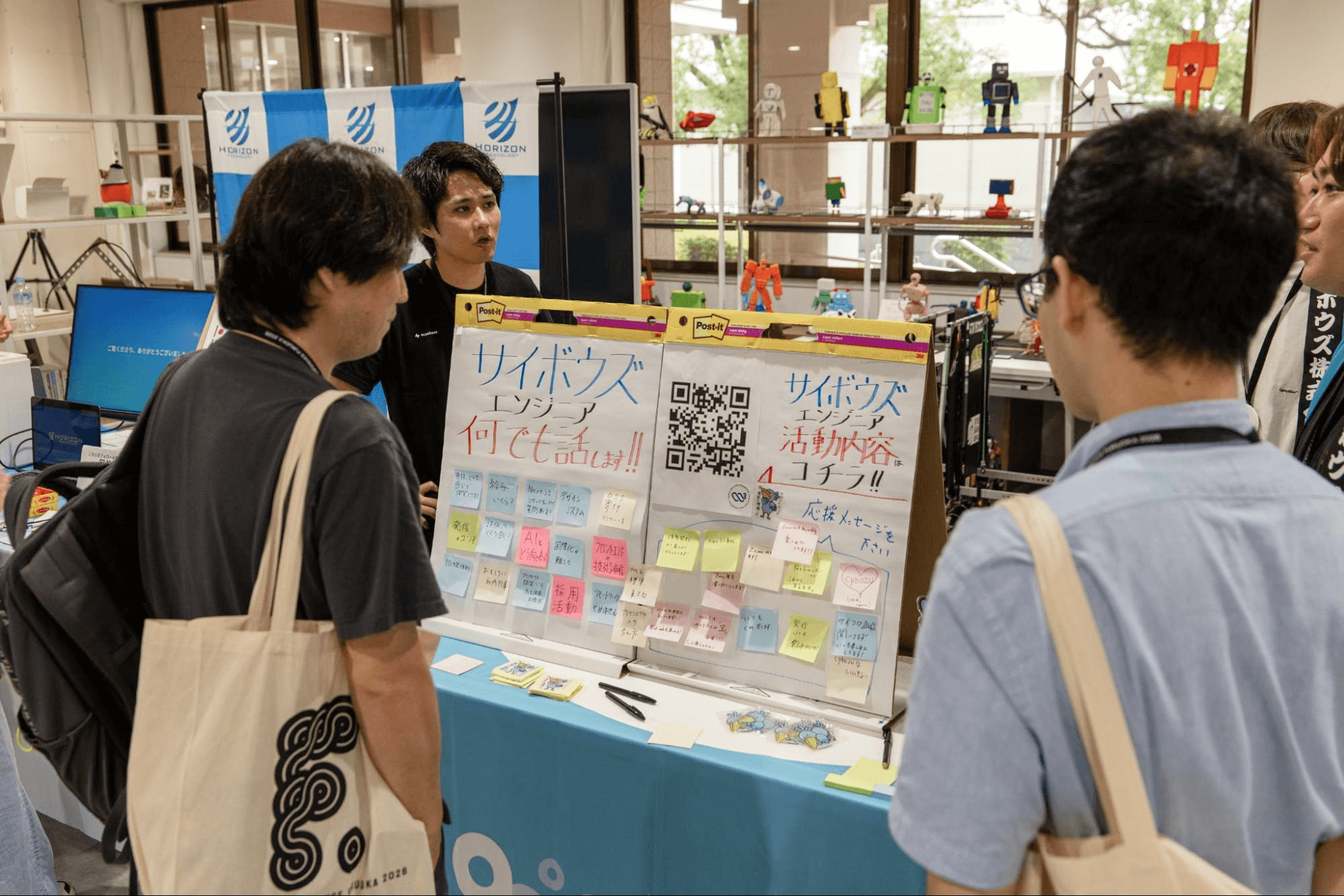 サイボウズのブースで、「何でも話します!!」と書かれた付箋ボードを前に参加者とブースのスタッフが話している様子